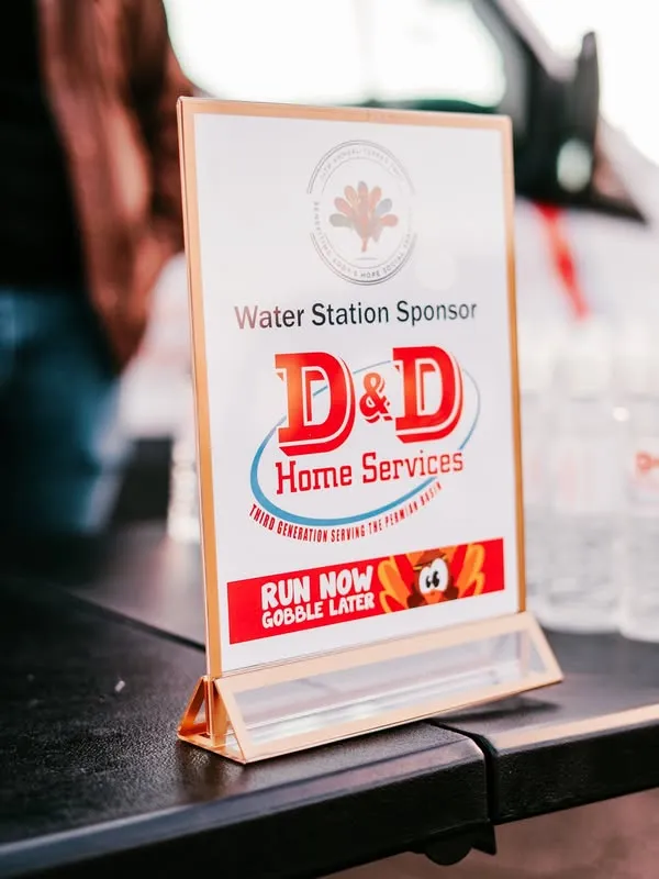 Tabletop sign advertising D&D Plumbing, Heating, and Air Conditioning as the water station sponsor with a cartoon banner reading 'Run Now Gobble Later'.