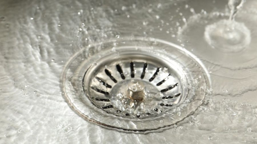 Close-up of a kitchen sink drain with standing water, illustrating a clogged drain or slow-draining sink that requires professional drain cleaning.