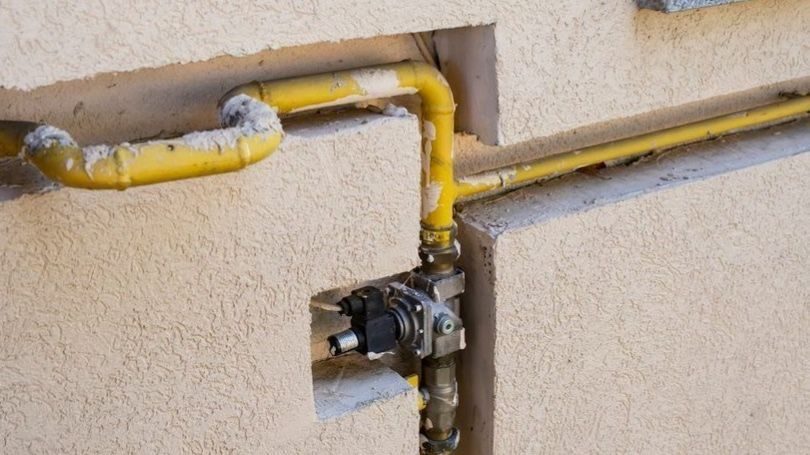 Gas line plumbing service showing an exterior natural gas pipe and shutoff valve installed along a residential home's stucco wall.